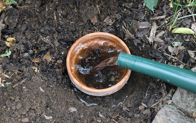 A terracotta pot in the ground filled with water 