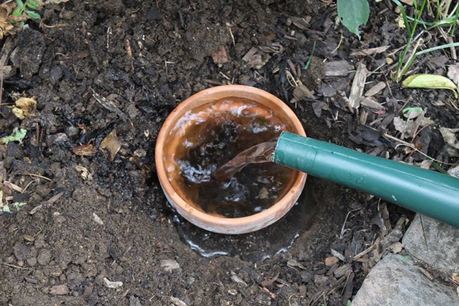 A terracotta pot in the ground filled with water 